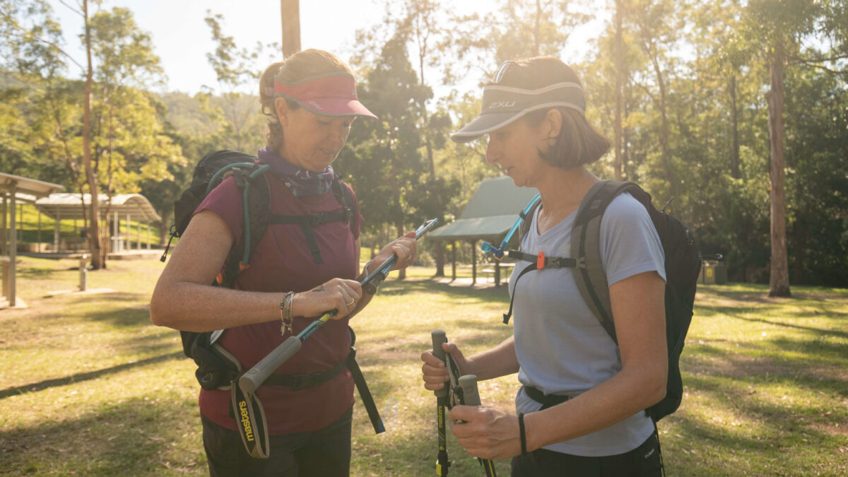 Two hikers adjusting trekking poles in a forest park
