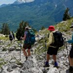 Women hikers trekking rocky mountain trail with gear