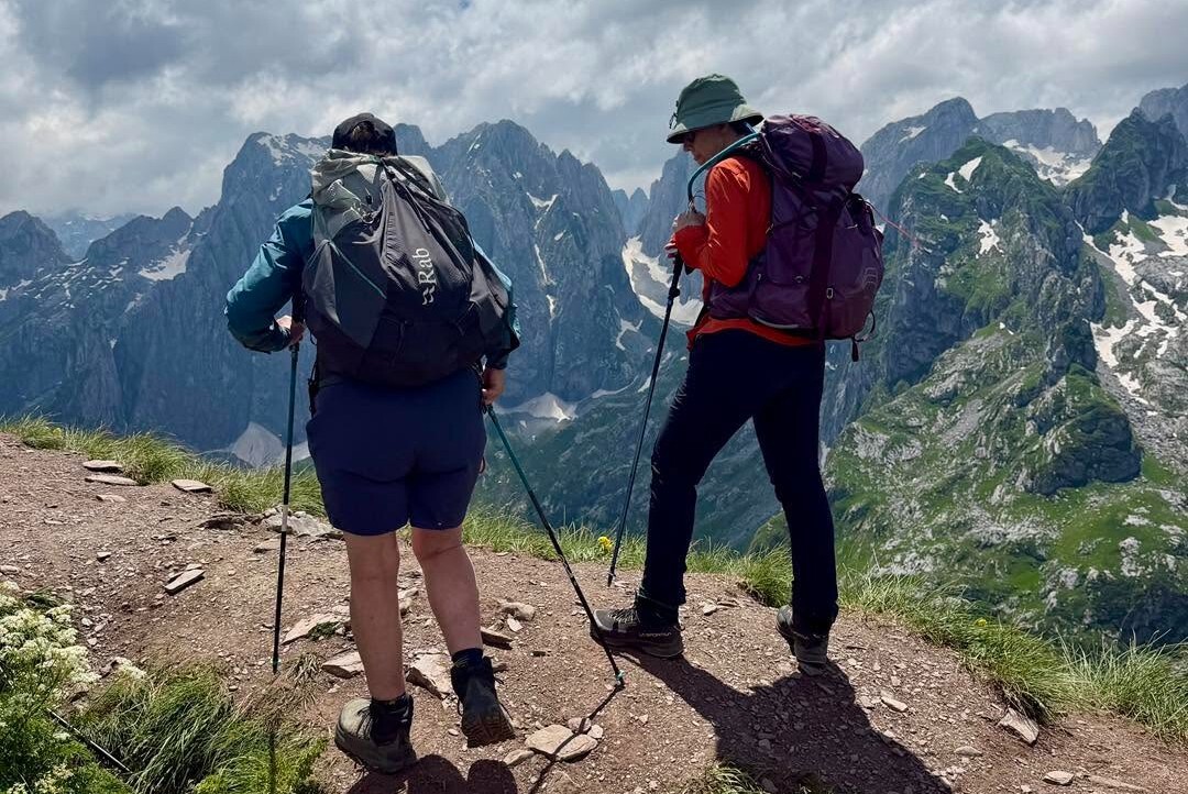 Two hikers trail mountain ridge overlooking snowy peaks